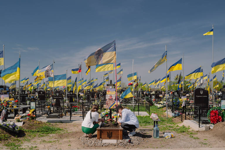 Familiares ajoelhados em frente a túmulo no cemitério Zakhdine, a oeste da cidade de Odessa, na Ucrânia