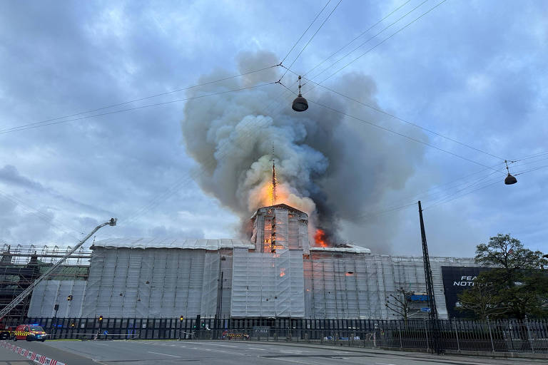 Fumaça e chamas se erguem de prédio cercado por tapumes