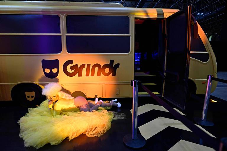 Drag queen fez performance no estande do Grindr, no Riocentro, em que há uma van amarela com o logo da empresa. Ela veste collant amarelo, com babados.