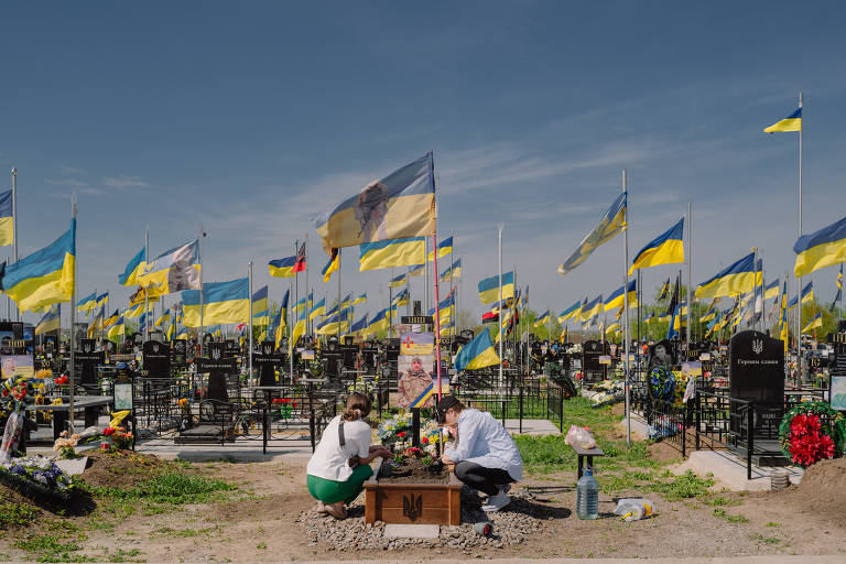 Familiares no Cemitério Zakhdine, no oeste de Odessa, na Ucrânia, ao lado do túmulo de um parente morto no conflito contra a Rússia; ucranianos vivem sob tensão enquanto tenta conciliar alertas contra foguetes com vida cotidiana
