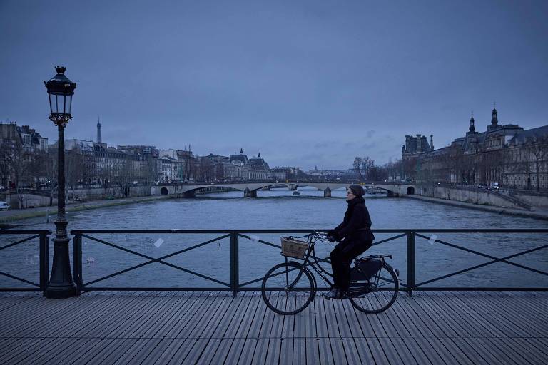 Mulher pedala em ponte sobre o rio em dia nublado