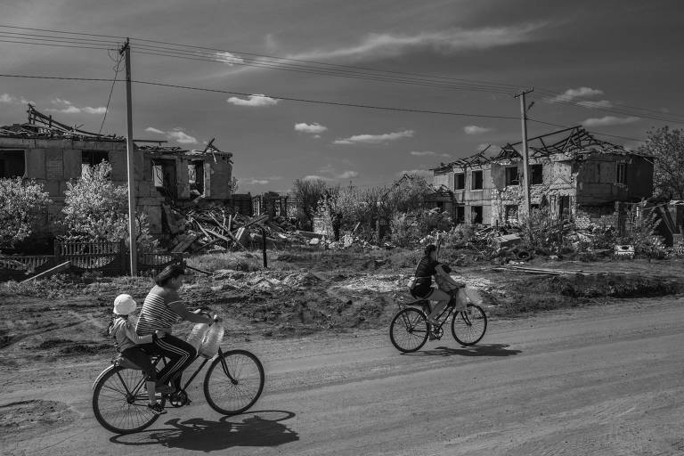 Pessoas passeiam de bicicleta em rua no vilarejo de Posa-Pokrovsk, na Ucrânia, em meio a construções destruídas