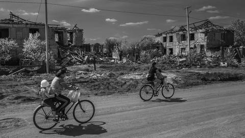 Odessa, Ucrânia - 14/4/2024 - Pessoas passam de bicicleta  por rua de terra batida em meio a casas destruídas por bombardeios no vilarejo de Posad-Pokrovs'ke, Ucrânia. (FOTO: FRANCISCO PRONER/Folhapress) * VENDA SOMENTE NO BRASIL*