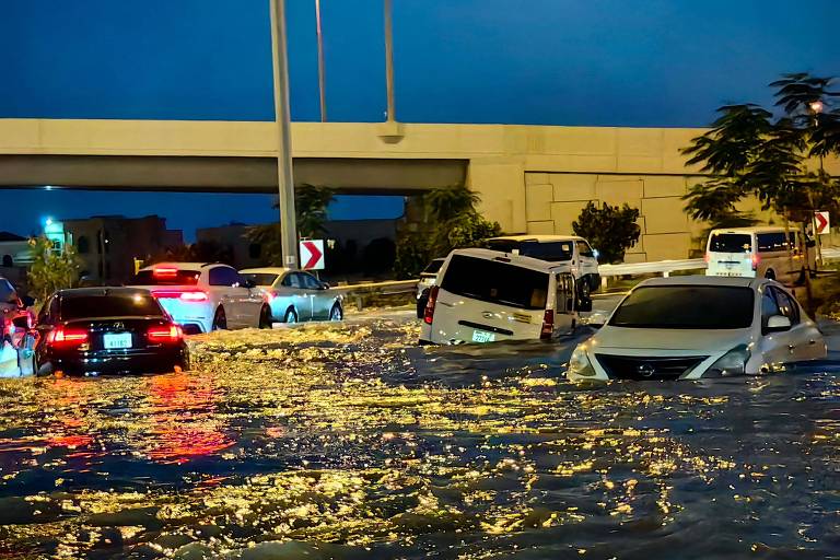 Carros passam por rua inundada por fortes chuvas em Dubai