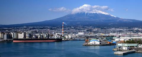This picture taken on March 22, 2024 shows clouds over Mount Fuji, Japan's highest mountain at 3,776 meters (12,388 feet), past industrial facilities at Tagonoura Port in Fuji city, Shizuoka Prefecture. (Photo by Philip FONG / AFP)