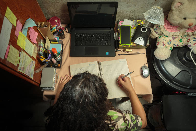 foto colorida mostra aluna estudando na mesa, com um computador, caderno