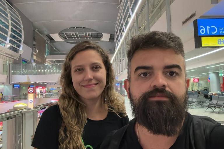 Homem com barba volumosa e mulher loira de cabelos compridos e ondulados posam para foto tipo "selfie" em aeroporto de Dubai