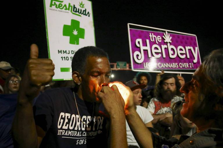 Homem, durante uma manifestação a favor da legalização da maconha, fuma um cigarro aceso por uma mulher