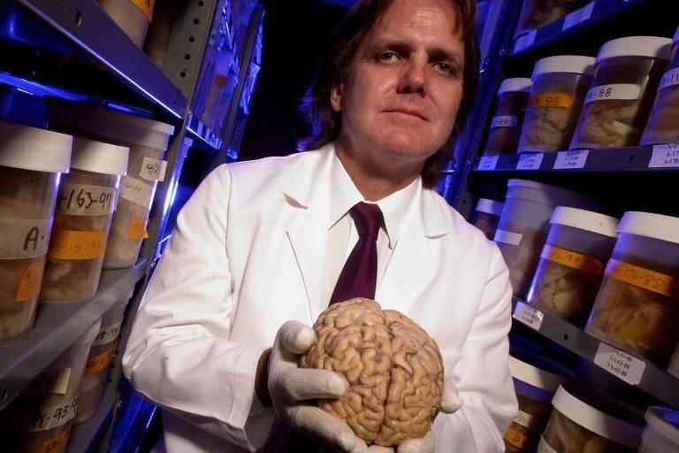 David Snowdon com um cérebro nas mãos, há prateleiras com outros cérebros atrás dele 