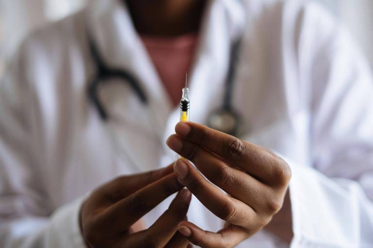 Mãos de uma médica negra segurando uma seringa de vacina