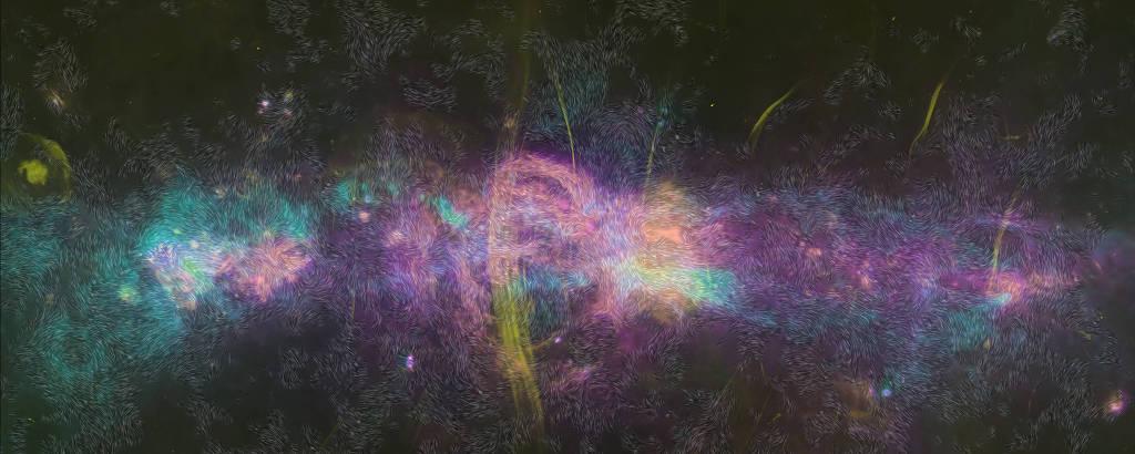 Espectro colorido e mapeamento do magnetismo interstelar. O fundo é predominantemente escuro, evocando o vasto espaço cósmico. No centro, um redemoinho de cores vibrantes, predominantemente em tons de azul, rosa e verde, simula as temperaturas da poeira interestelar. Linhas sinuosas, semelhantes a pelos ou fibras, se estendem por toda a imagem em padrões complexos, representando as direções da força magnética nas nuvens de poeira. Faixas amarelas, lembrando jatos ou riscos, cortam a cena, simbolizando jatos de gás ionizado quente que emitem ondas de rádio. A imagem é uma composição artística baseada em dados astronômicos e transmite uma sensação de dinamismo e complexidade dos processos cósmicos.