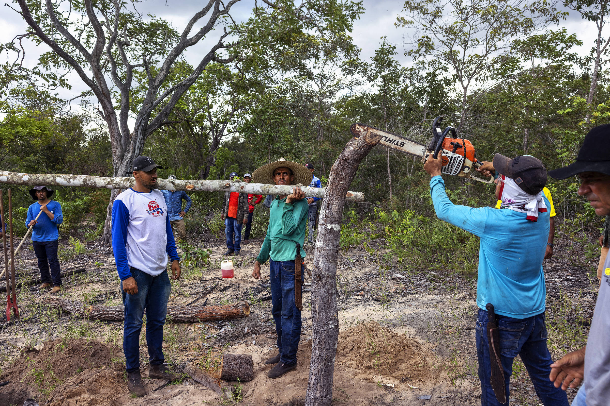 Grupo de oito homens serram madeira para reconstruir rancho