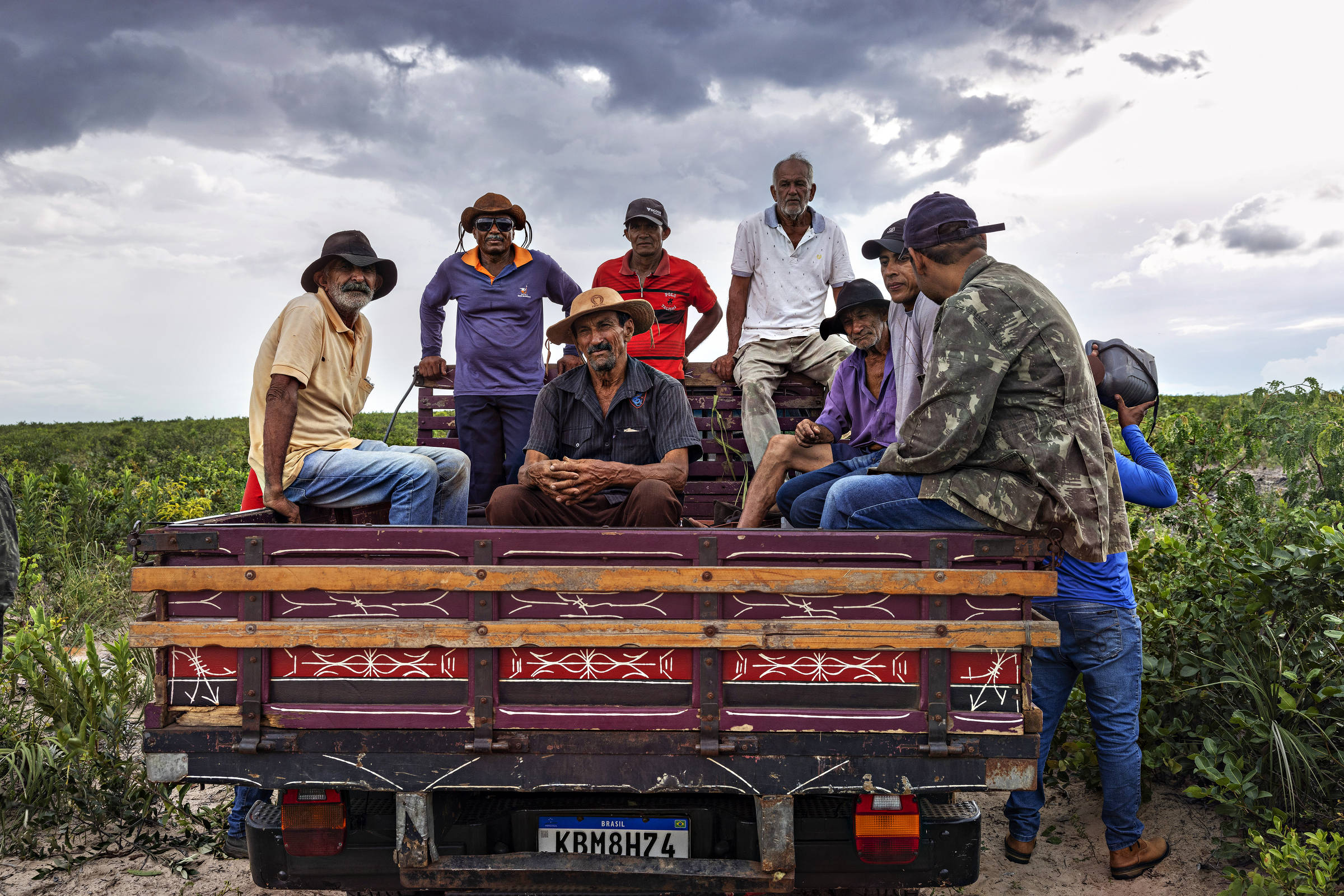 Grupo de agricultores sentados em caçamba de pau de arara em meio ao cerrado