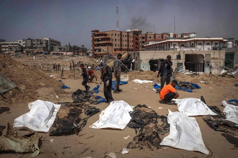Palestinos próximos de corpos desenterrados de vala comum no complexo do hospital Nasser, em Gaza