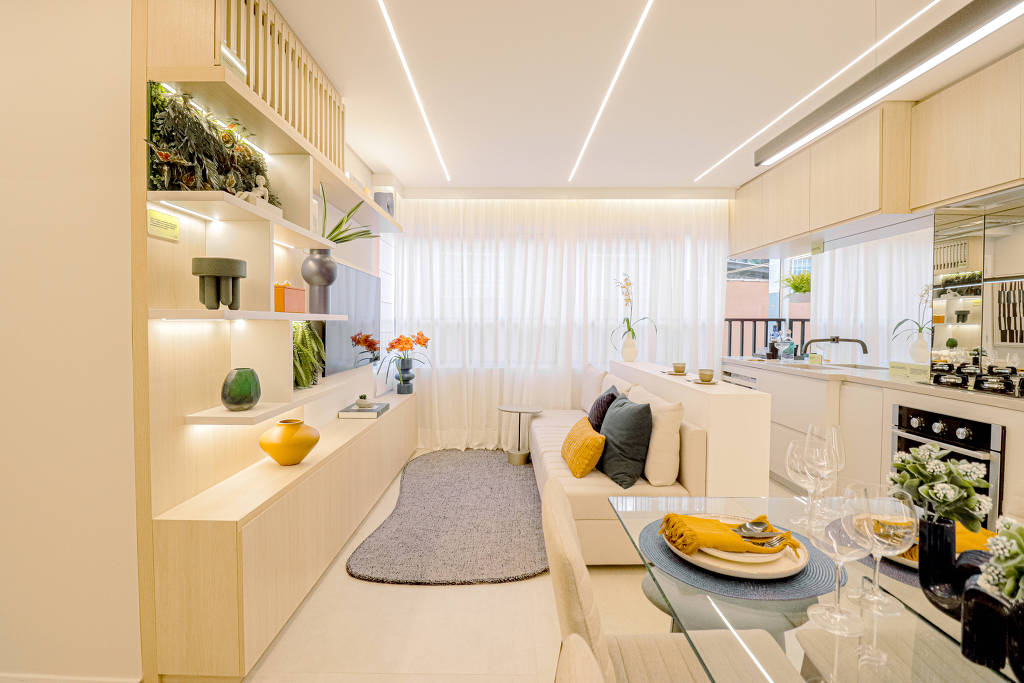sala clara, com móveis em madeira clara, sofá branco de frente para uma tv com prateleiras ao lado