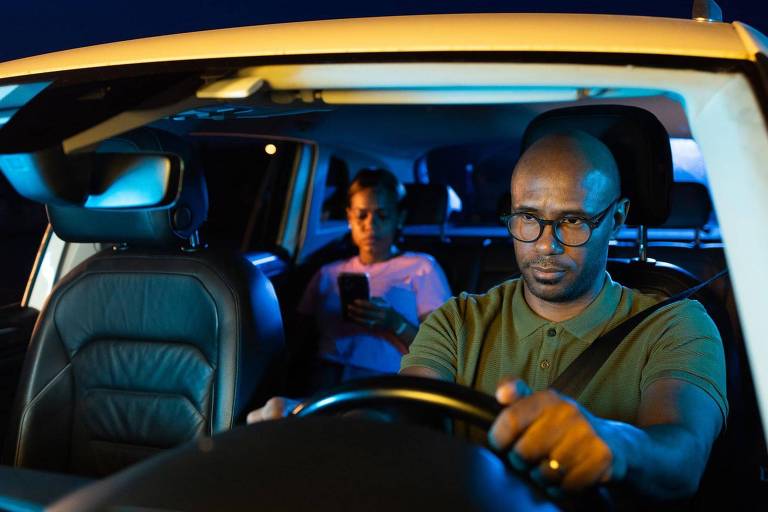 Homem dirigindo carro de aplicativo com passageira à noite