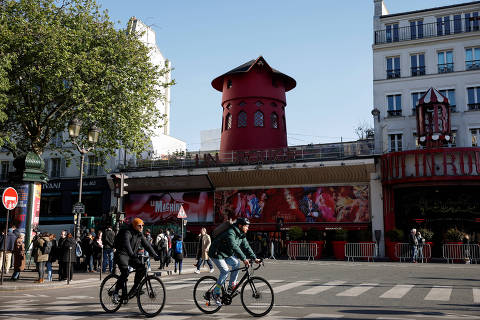 Cyclists pass by the landmark red windmill atop the Moulin Rouge, Paris' most famous cabaret club, after its sails fell off during the night in Paris, France, April 25, 2024. REUTERS/Benoit Tessier ORG XMIT: GGG-BTE24