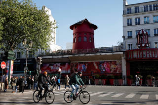 Cyclists pass by the landmark red windmill atop the Moulin Rouge, Paris' most famous cabaret club, after its sails fell off during the night in Paris