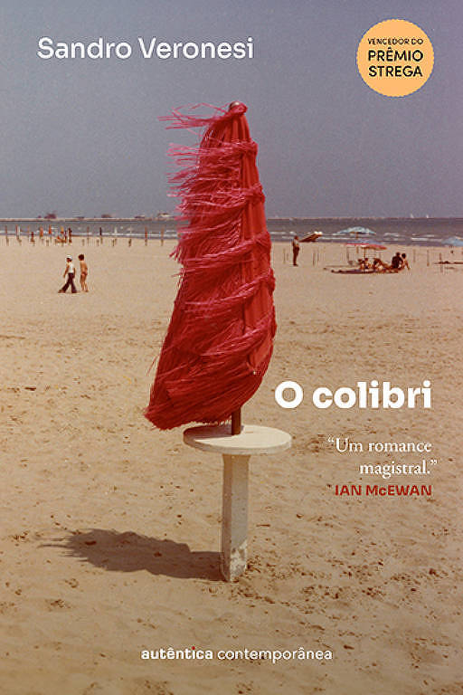 Capa do livro O colibri mostra guarda-sol vermelho fechado em uma praia pouco movimentada