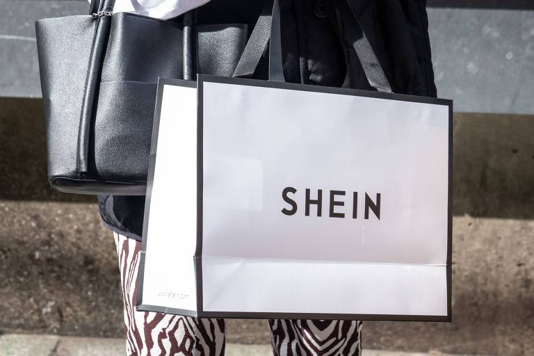 Uma mulher segura uma sacola de compras Shein do lado de fora do primeiro showroom permanente da gigante chinesa de fast fashion online Shein no dia de inauguração da loja em Tóquio, em 13 de novembro de 2022