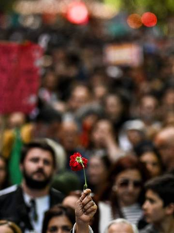 TOPSHOT - A woman holds a red carnation as people demonstrate during the Carnation Revolutions 50th anniversary at Avenida da Liberdade in Lisbon on April 25, 2024. Portugal marks the 50th anniversary of the Carnation Revolution, a military coup that put an end to Europe's longest-lived dictatorship and 13 years of colonial wars in Africa. (Photo by PATRICIA DE MELO MOREIRA / AFP)