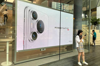 A woman uses her cellphone while standing in front of a screen advertising Huawei Pura 70 series smartphones outside Huawei's flagship store in Shenzhen