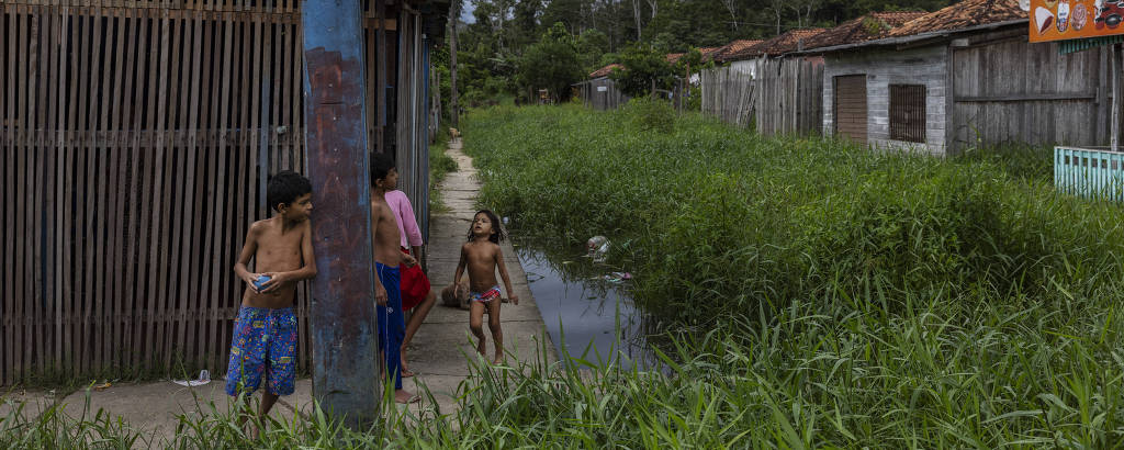 Crianças brincam em uma rua coberta por vegetação em Cidade de Deus, um conjunto habitacional não concluído na periferia de Breves, na Ilha do Marajó, que foi invadido por famílias de baixa renda