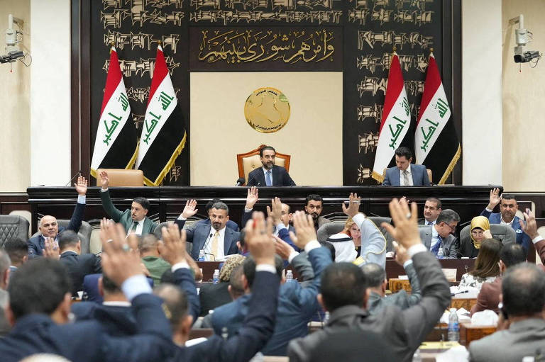 Homens de terno com as mãos levantadas com bandeiras do Iraque ao fundo