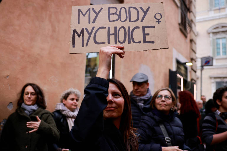 Mulheres seguram cartazes e uma eles diz "Meu corpo, minhas escolhas". 