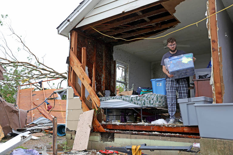 Homem carrega caixa em casa com parede destruída