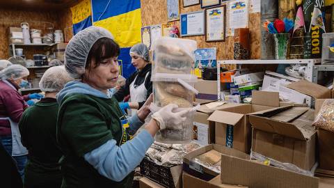 Kyiv, Ucrânia - 17/4/2024 -   Voluntária carrega pilha de potes com alimentos desidratados na sede do projeto 