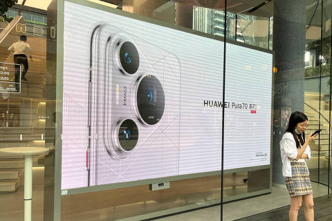 A woman uses her cellphone while standing in front of a screen advertising Huawei Pura 70 series smartphones outside Huawei's flagship store in Shenzhen, China April 26, 2024. REUTERS/David Kirton ORG XMIT: PPP-CH001