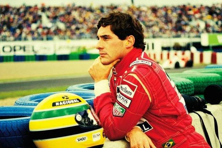 Em foto envelhecida, piloto Ayrton Senna observa pista de corrida ao lado de seu capacete
