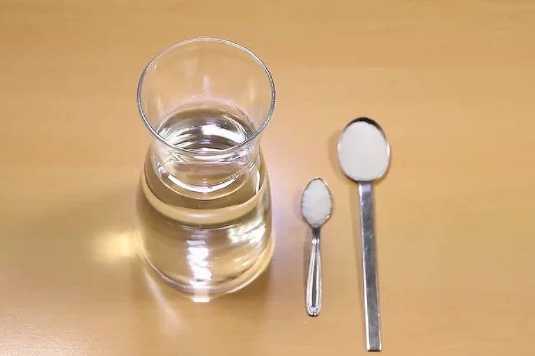 Copo de água ao lado de uma colher de chá de sal e uma colher de sopa de açúcar