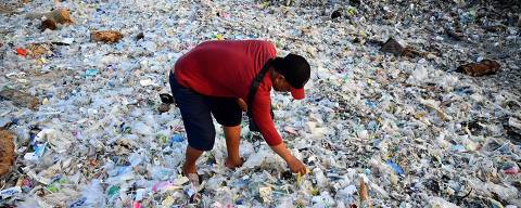TOPSHOT - A man looks through plastic and other debris washed ashore at Kedonganan Beach near Denpasar on Indonesia's resort island of Bali on March 19, 2024. (Photo by SONNY TUMBELAKA / AFP)