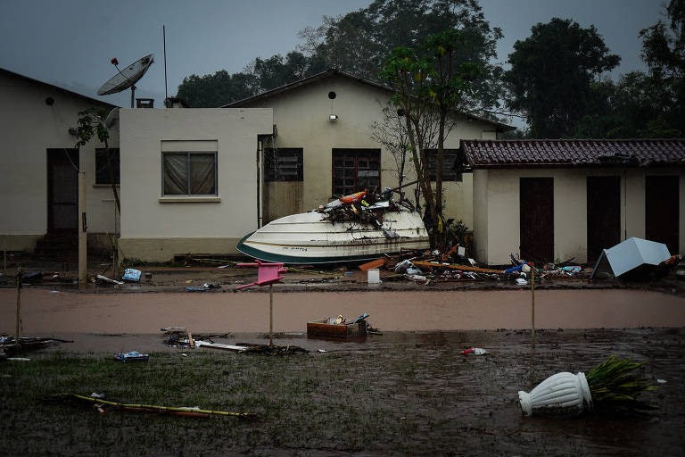 Barco virado em frente a uma casa e destroços deixados após chuvas no Rio Grande do Sul
