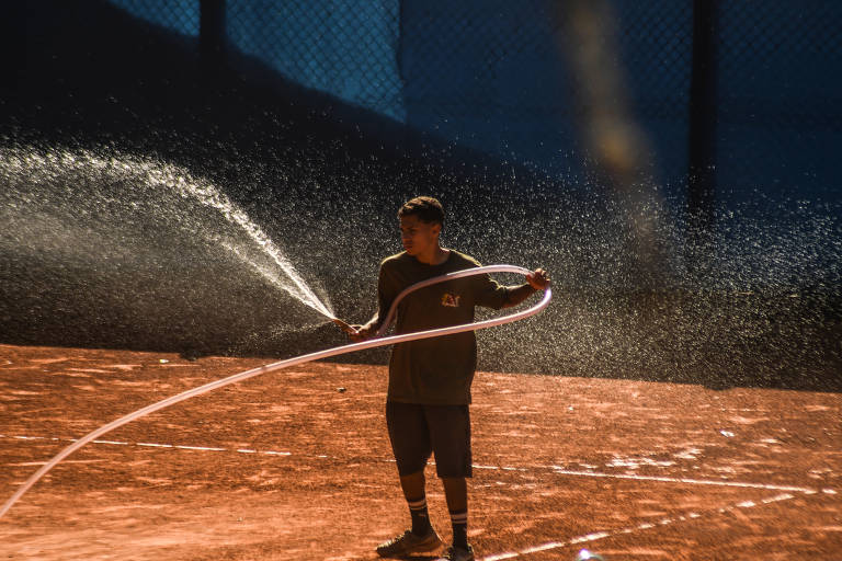 Homem molha uma das várias quadras de tênis do espaço