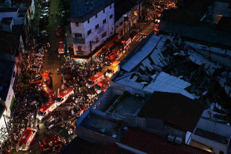 a foto aérea mostra o teto desabado da igreja à noite, numa região lotada de pessoas e ambulâncias