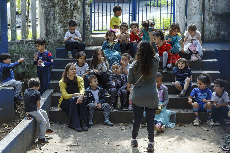 Crianças e professoras sentados em degraus de um pátio