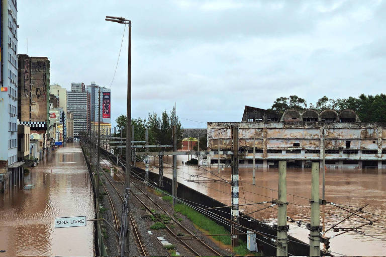 Na foto, um trilho de trem parciamente inundado corta uma cidade alagada nos dois lados