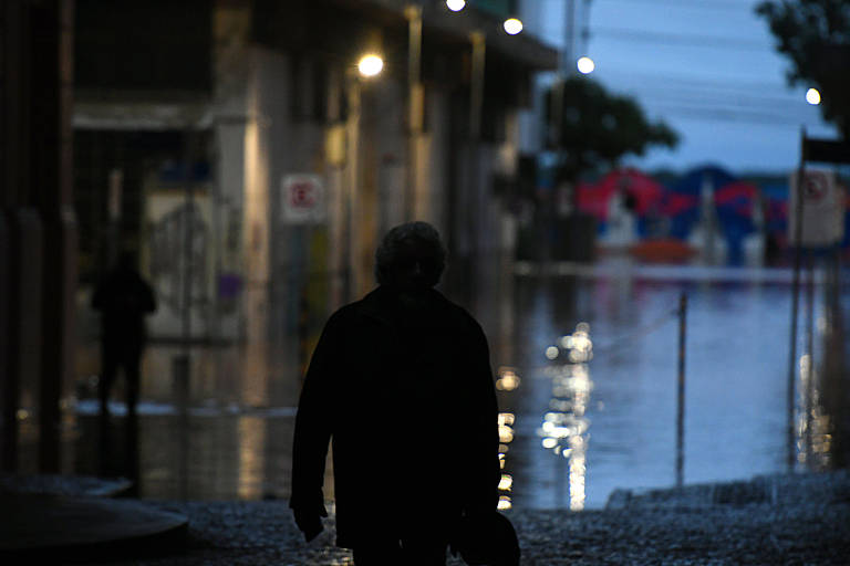Na foto, aparece a silhueta de um homem de costas, olhando a água tomando conta de uma rua no centro de Porto Alegre