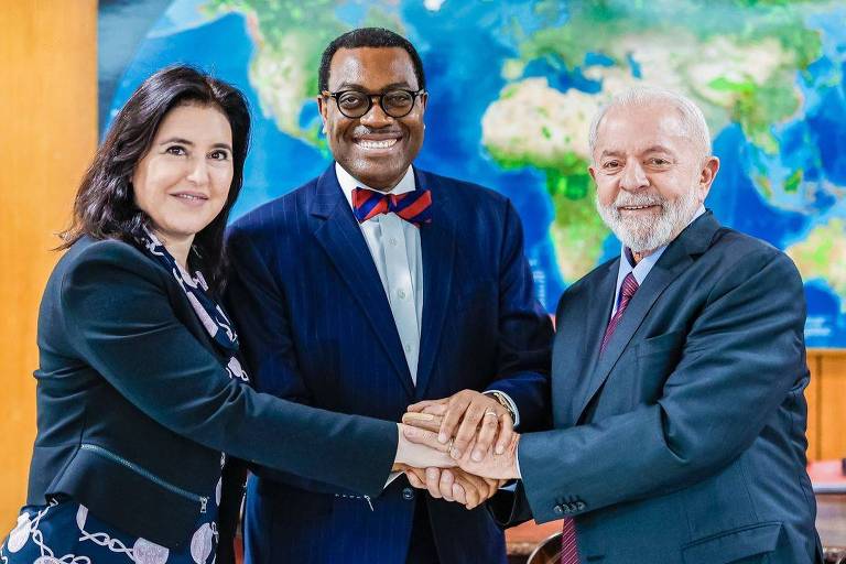 Ministra Simone Tebet (Planejamento e Orçamento), à esquerda, e presidente Lula, à direita, dão as mãos ao presidente do Banco Africano de Desenvolvimento, Akinwumi Adesina, que está no centro da foto