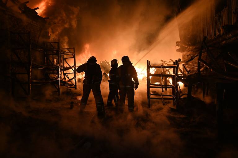 Bombeiros trabalham em um local em chamas com bastante fumaça.
