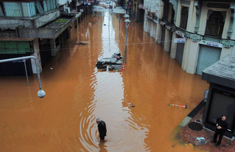 Uma visão de drone mostra o centro de uma cidade inundada com um homem caminhando com água até os joelhos.