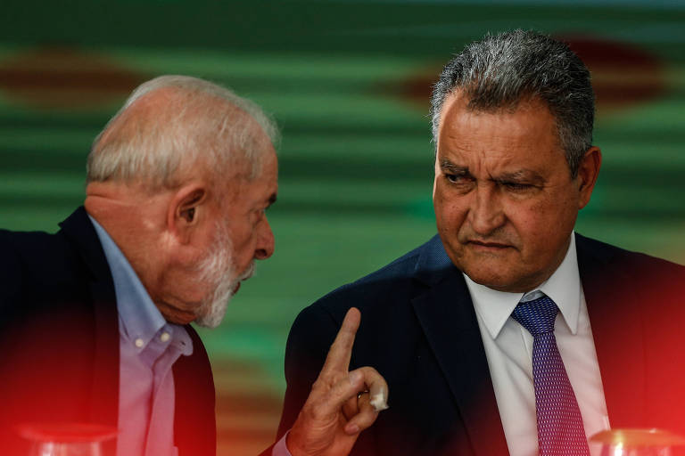 Lula e Rui Costa envolvidos em uma conversa séria. O homem à esquerda, com cabelos brancos e barba, parece estar fazendo um ponto enfático, enquanto o homem à direita, com cabelos grisalhos e bigode, ouve atentamente com uma expressão de seriedade.