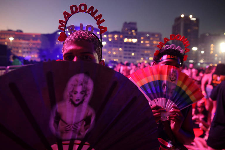 fãs são retratados segurando leques com a foto de madonna e as cores do arco íris em meio a multidão.