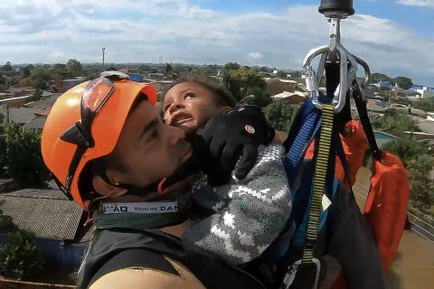 This handout frame grab from a video released by the Brazilian Navy on May 6, 2024 shows a Brazilian Navy member rescuing a child by helicopter at Mathias Velho neighbourhood, in Canoas, Rio Grande do Sul State, Brazil, on May 5, 2024. From top to bottom, rescuers scour buildings in Porto Alegre for inhabitants stuck in apartments or on rooftops as unprecedented flooding killed at least 78 people in the southern state, with dozens missing and some 115,000 forced to leave their homes. (Photo by Handout / BRAZILIAN NAVY / AFP) / RESTRICTED TO EDITORIAL USE - MANDATORY CREDIT 
