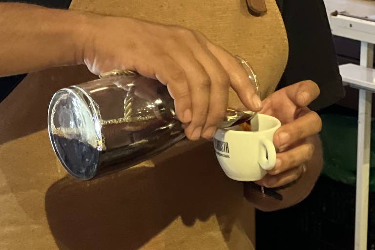 Pessoa serve café de uma jarra de vidro em uma pequena xícara