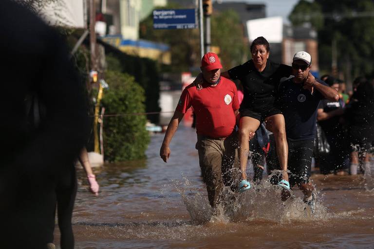 Bombeiro e voluntário carregam mulher resgatada de área atingida por enchente em Porto Alegre 