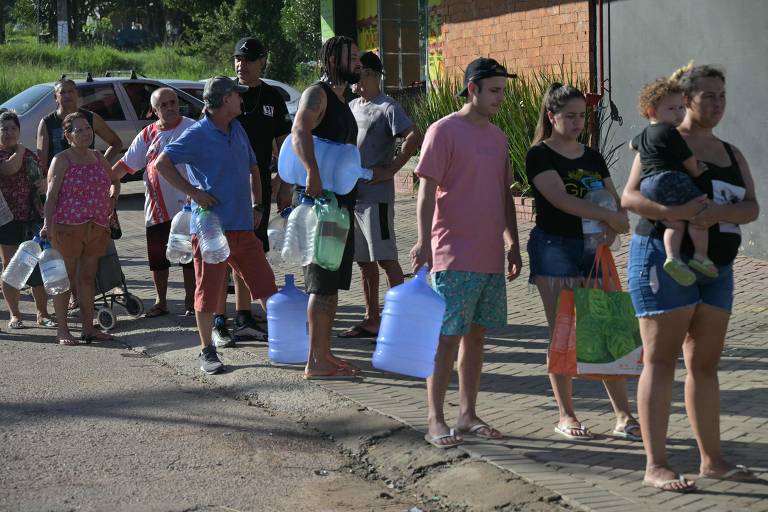 Pessoas segurando galões de água vazios formam fila em uma calçada